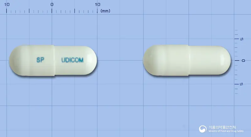 유디콤캡슐 앞뒤 사진 (흰색 캡슐, 각인 SP UDICOM)